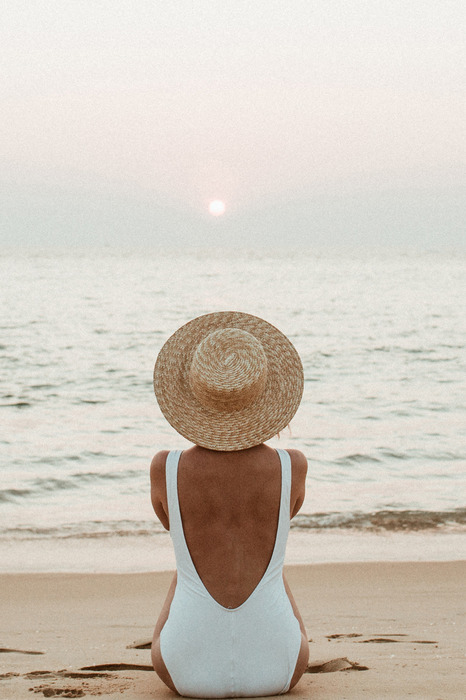 Eine frau mit hut sitzt am meer