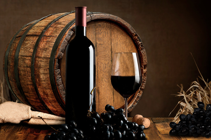 Une bouteille de vin rouge et un verre sur fond de tonneau en bois