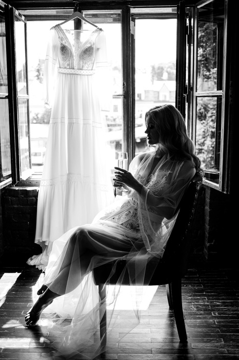 Femme à la fenêtre avec une robe de mariée suspendue