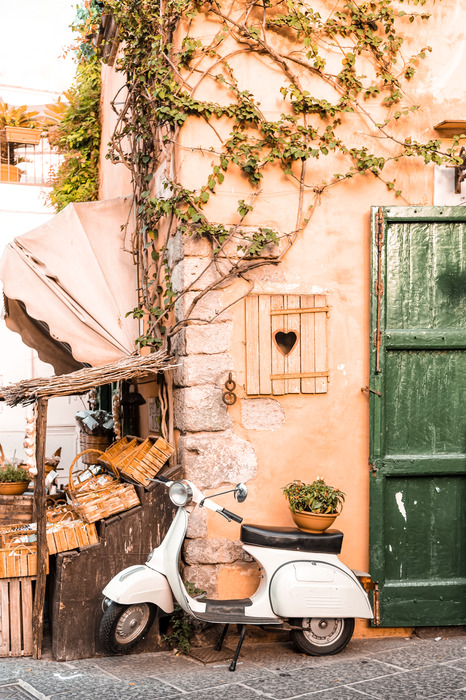 Un scooter blanc avec un bâtiment recouvert de vigne en arrière-plan