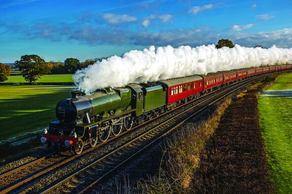 Een stoomlocomotief die door groene velden rijdt