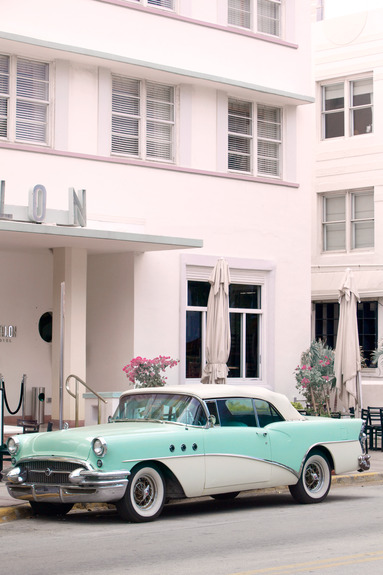 Een blauwe klassieke auto voor een roze hotel