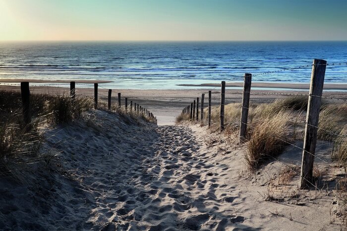 Een zandpad richting de blauwe golven van de zee
